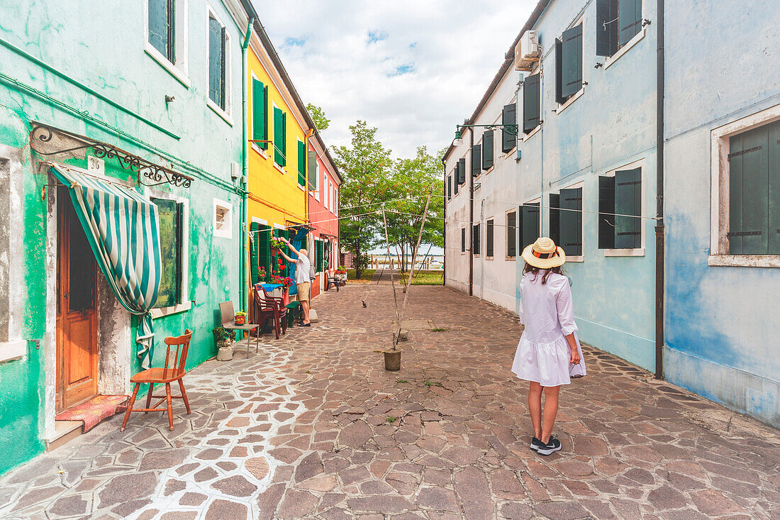 A woman in the middle of rows of colorful buildings in Burano, Venice, Veneto, Italy, Europe