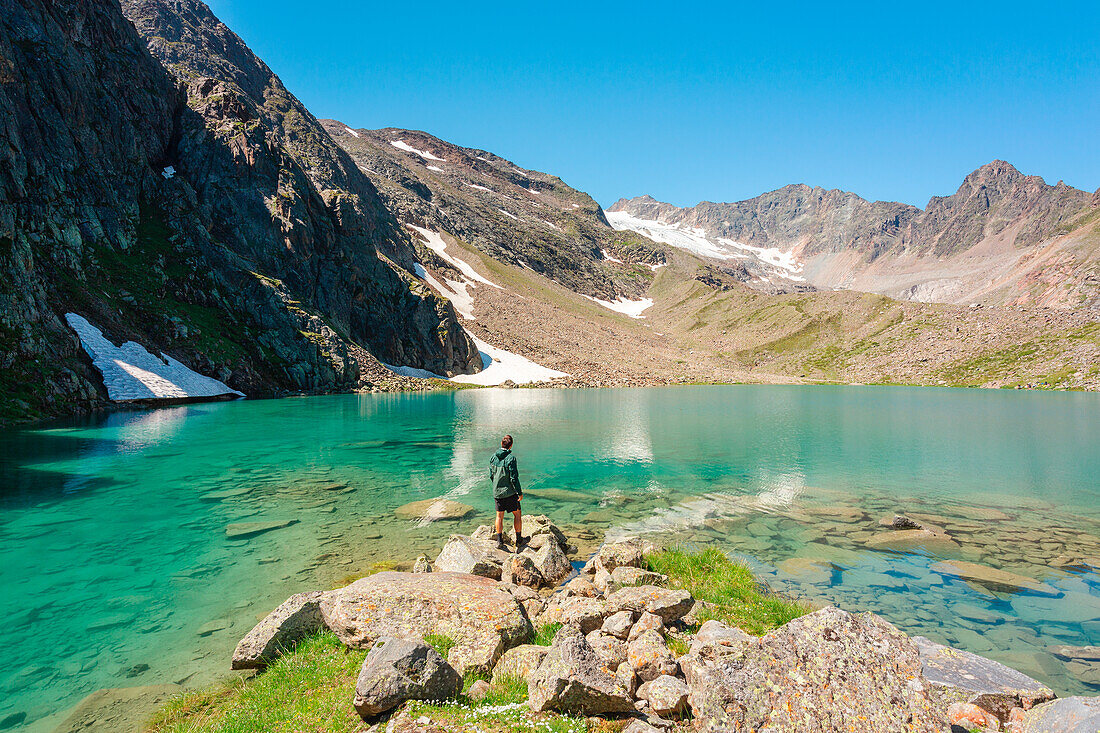 A Mountaineer staring at the turquoise waters of Blaue Lacke mountain lake with the glacier of Sulzenau in the background, Neustift im Stubaital, Innsbruck Land, Tyrol, Austria, Europe