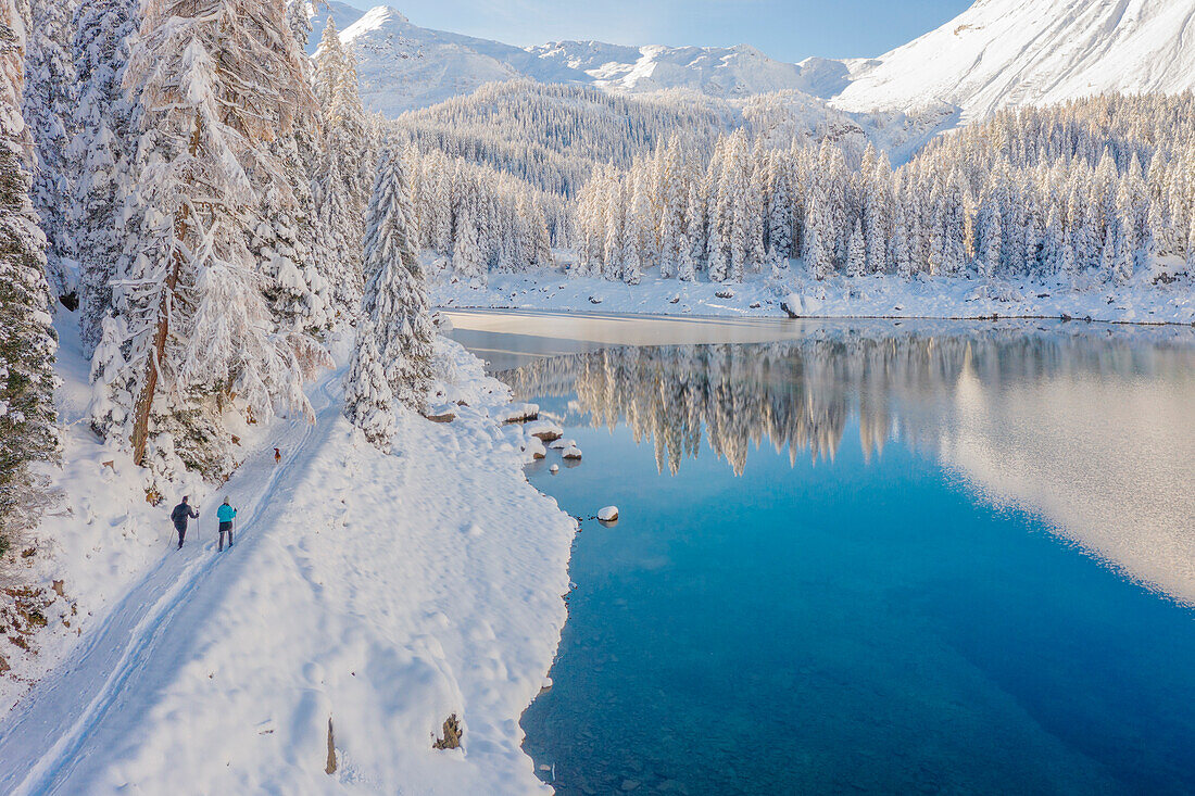 Luftaufnahme von zwei Wanderern und einem Hund, die nach starkem Schneefall um den Obernberger See wandern, Obernberg am Brenner, Innsbrucker Land, Tirol, Österreich, Europa