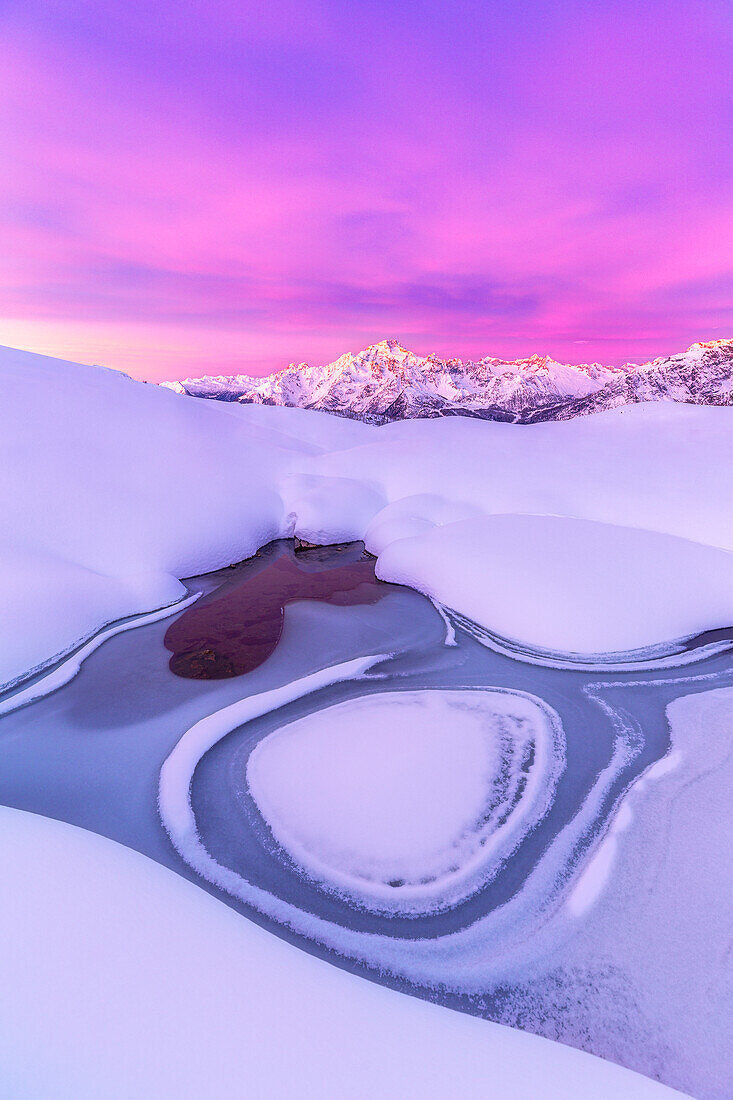 Verrückte Form in einem zugefrorenen Alpensee bei Sonnenaufgang mit Blick auf den Monte Disgrazia. Valmalenco, Valtellina, Lombardei, Italien, Europa
