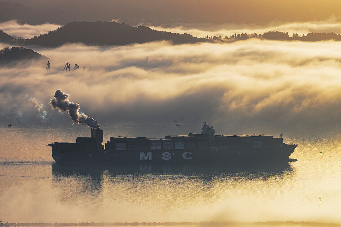 Container ship maneuvering in the port of La Spezia submerged by maritime fog, La Spezia province, Liguria district, Italy, Europe.