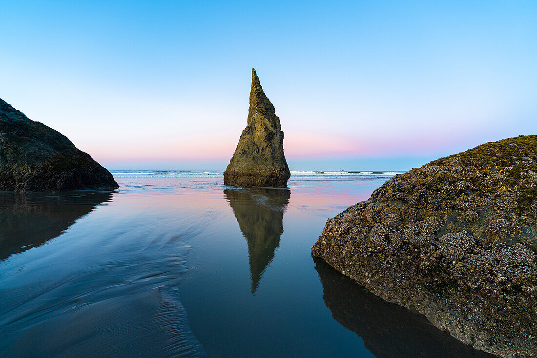 Der Wizard's Hat Sea Stack spiegelt sich bei Ebbe am Bandon Beach in der Morgendämmerung. Bandon, Landkreis Coos, Oregon, USA.