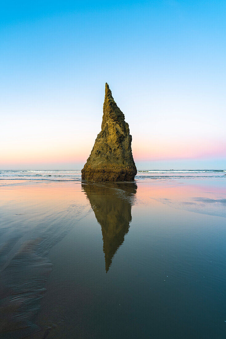 The Wizard's hat sea stack reflecting on low tide on Bandon Beach at dawn. Bandon, Coos county, Oregon, USA.