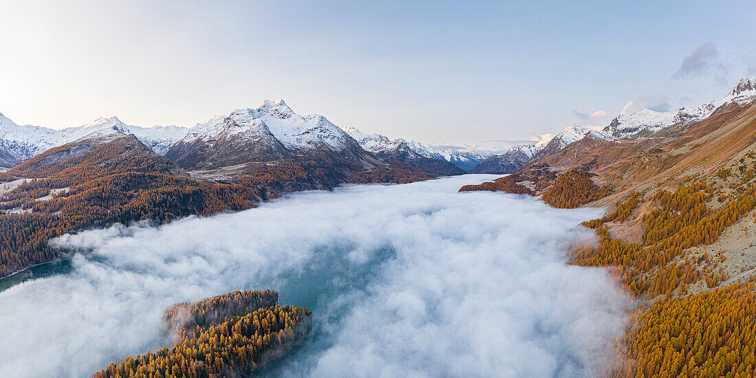 Schweiz, Kanton Graubünden, Region Maloja, Sils im Engadin/Segl: Drohnenaufnahme von tief hängenden Wolken über dem Silsersee, mit dem schneebedeckten Gipfel der La Margna im Hintergrund, im Herbst.