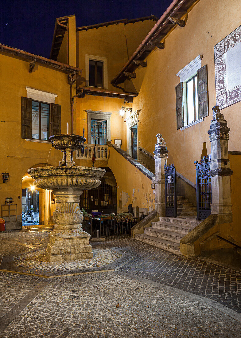 Der kleine Platz mit seinem Brunnen in einem mittelalterlichen Dorf in den Abruzzen wird von künstlichen Lichtern beleuchtet. Pettorano sul Gizio, Provinz L'Aquila, Abruzzen, Italien, Europa