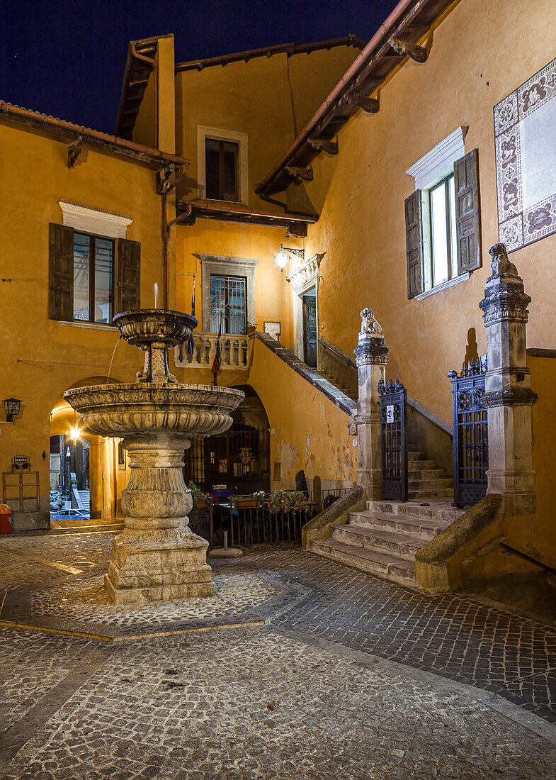 The small square with its fountain in a medieval village in Abruzzo is illuminated by artificial lights. Pettorano sul Gizio, province of L'Aquila, Abruzzo, Italy, Europe