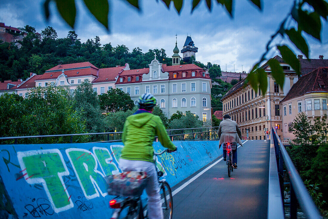 Cityscape with Schlossberg or Castle Hill mountain with old clock tower Uhrturm, from a bridge over the Mur river, Graz