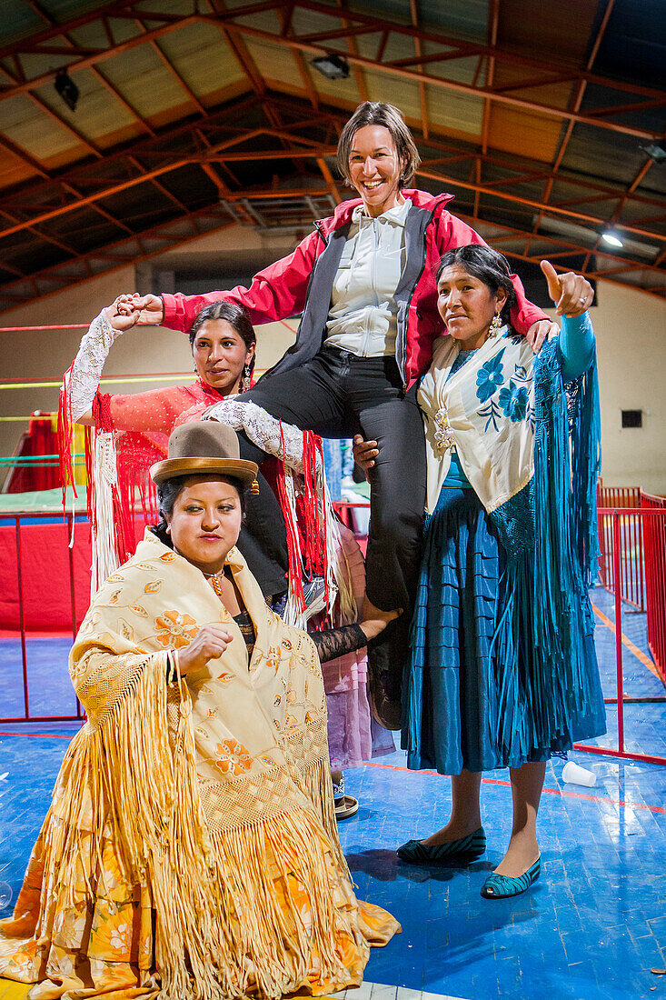 Lucha Libre. After the show. A follower is photographed with cholitas fighters. Down Julieta, Celia la Simpatica, and Dina with blue dress , cholitas females wrestlers ,Sports center La Ceja, El Alto, La Paz, Bolivia