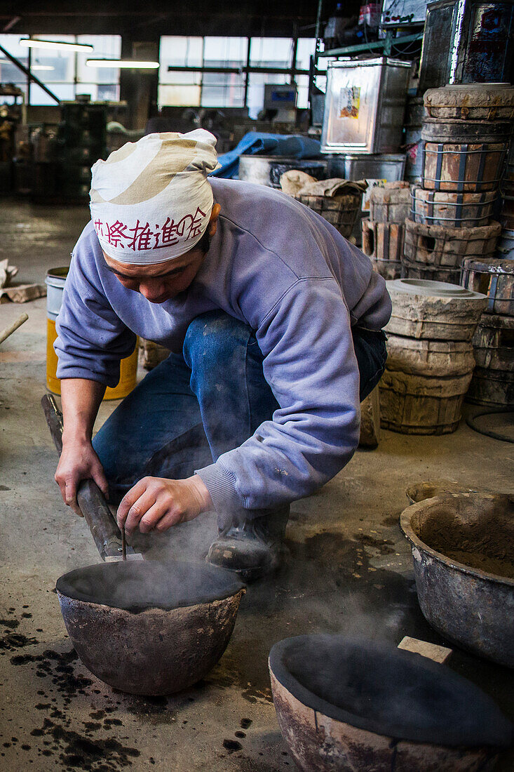 Takahiro Koizumi bereitet einen Löffel vor, um geschmolzenes Eisen in eine Form zu füllen, um eine eiserne Teekanne oder Tetsubin herzustellen, nanbu tekki, Werkstatt der Familie Koizumi, Morioka, Präfektur Iwate, Japan