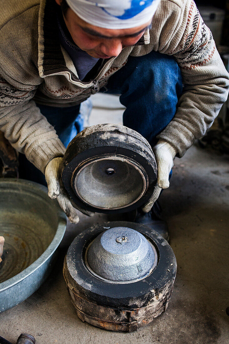 Takahiro Koizumi öffnet die Form, kurz nachdem das geschmolzene Eisen erstarrt ist. Er wirft den ersten Blick auf die neue eiserne Teekanne oder Tetsubin, nanbu tekki, Werkstatt der Familie Koizumi, Handwerker seit 1659, Morioka, Präfektur Iwate, Japan