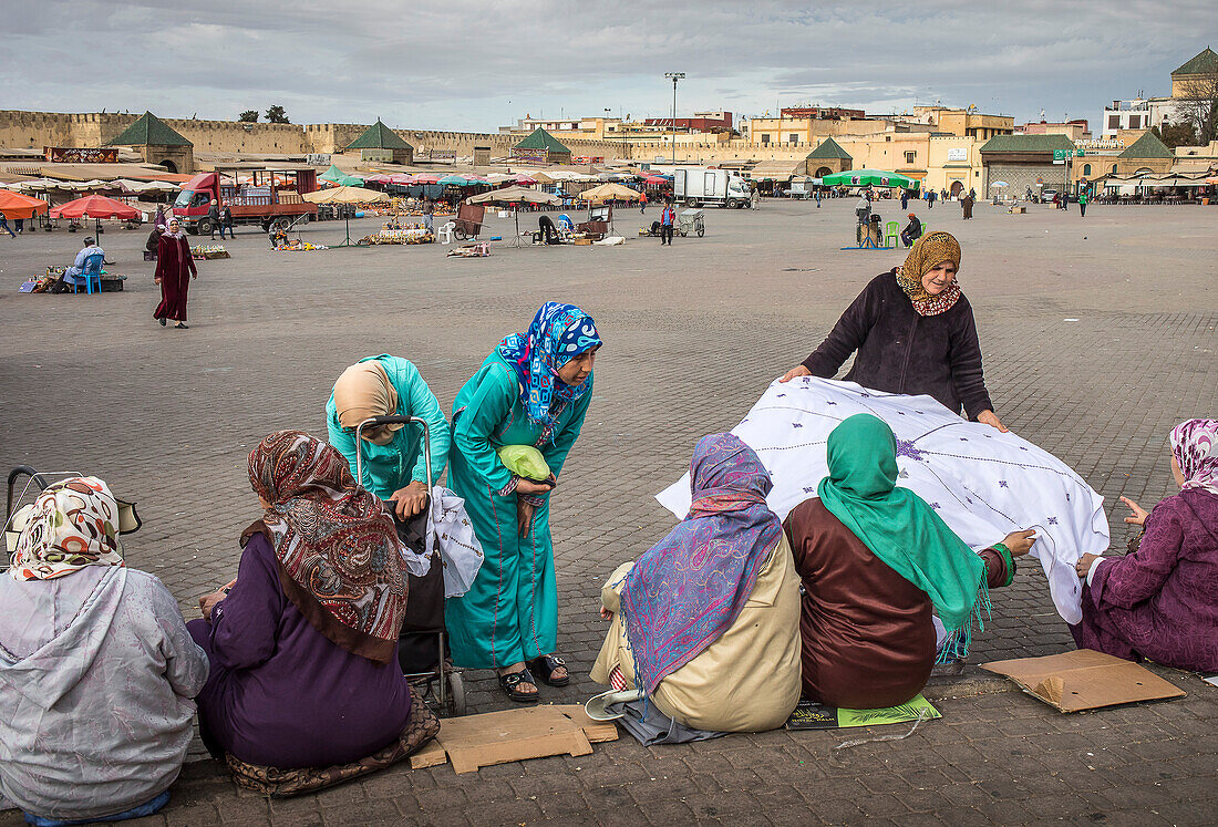 Frauen und Männer verkaufen handgefertigte Tischtücher mit traditionellen Motiven. Auf dem El Hedim-Platz, Meknes, Marokko