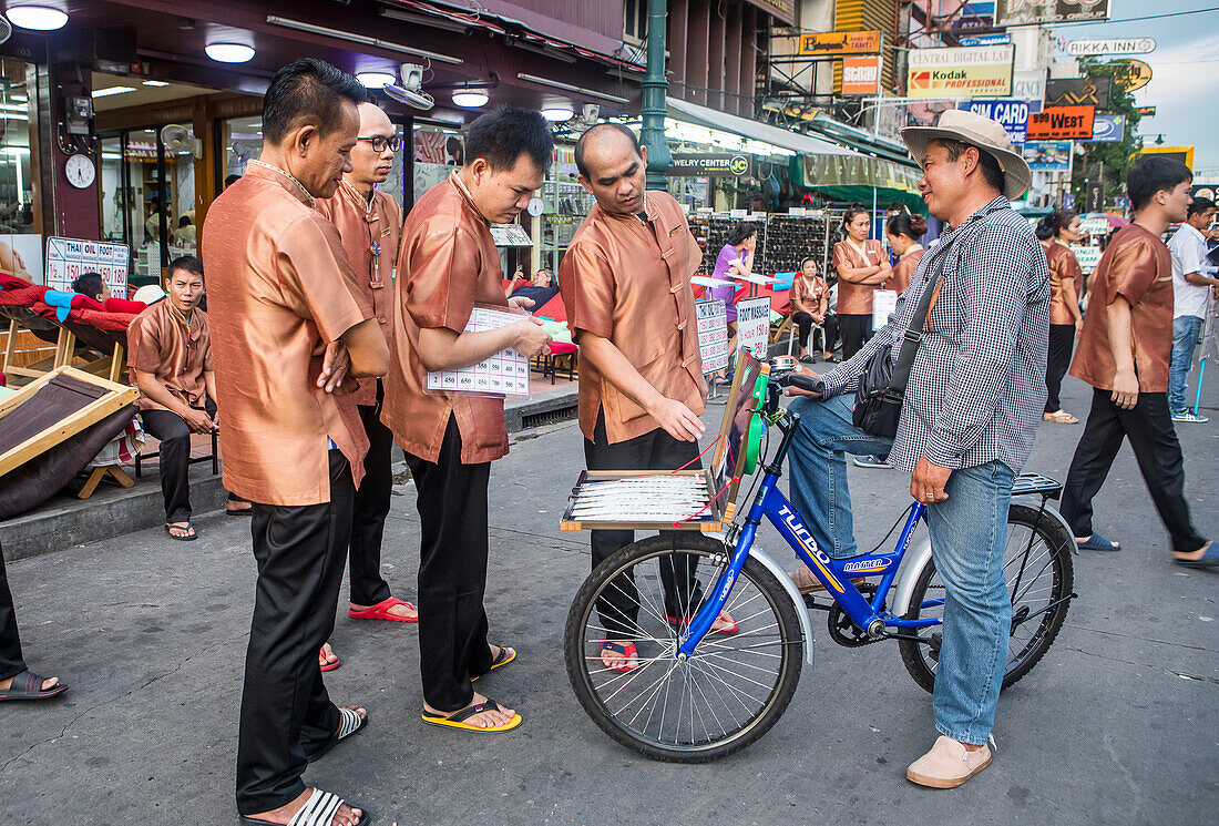 Lottery salesman shows his numbers to workers of a massage studio, in Khao San Road, Bangkok, Thailand