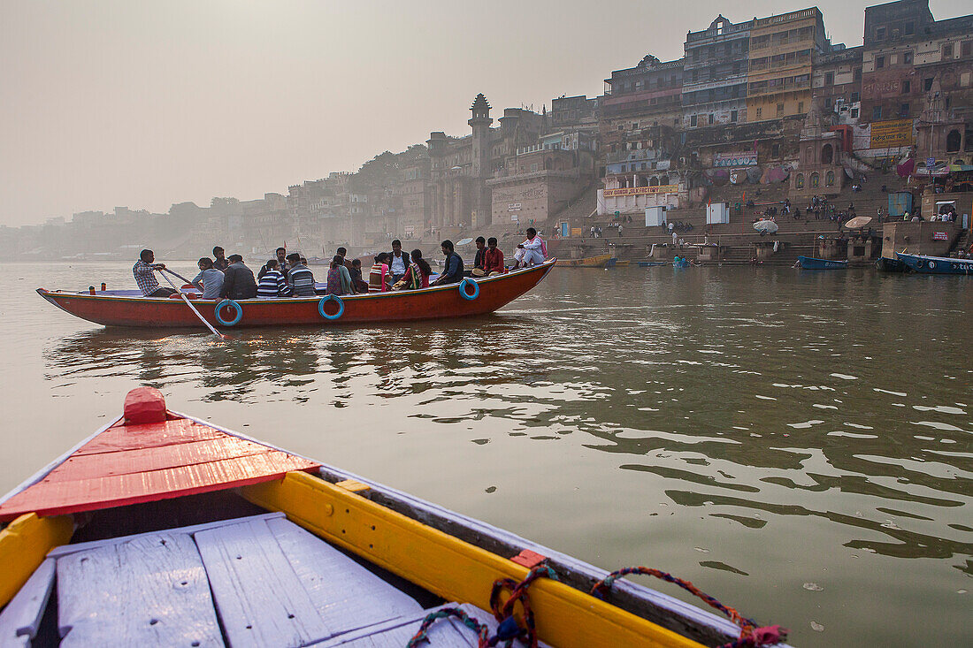 Pilger in einem Boot beim Segeln und Beten, Fluss Ganges, im Hintergrund die Ghats, Varanasi, Uttar Pradesh, Indien.