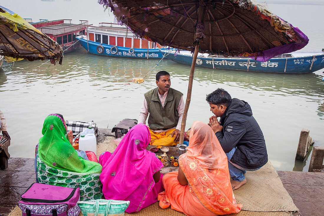 Pilger und ein Pandit (heiliger Mann und Priester, der Zeremonien durchführt), der eine Puja (Gebet) leitet, an den Ghats des Ganges, Varanasi, Uttar Pradesh, Indien.