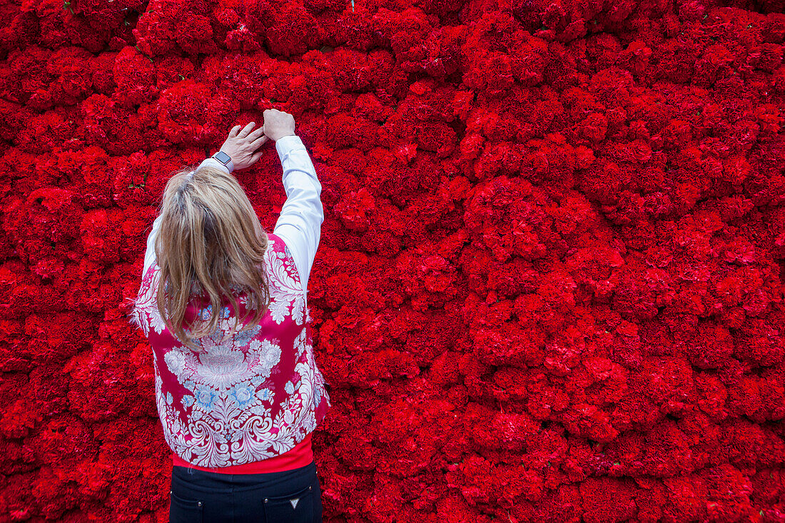 Woman placing flower offerings on large wooden replica statue of Virgen de los Desamparados, Fallas festival,Plaza de la Virgen square,Valencia