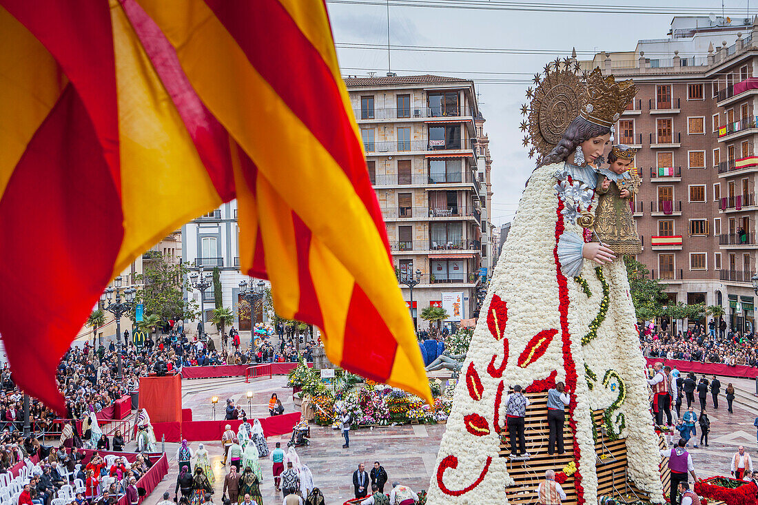 Men placing flower offerings on large wooden replica statue of Virgen de los Desamparados, Fallas festival,Plaza de la Virgen square,Valencia