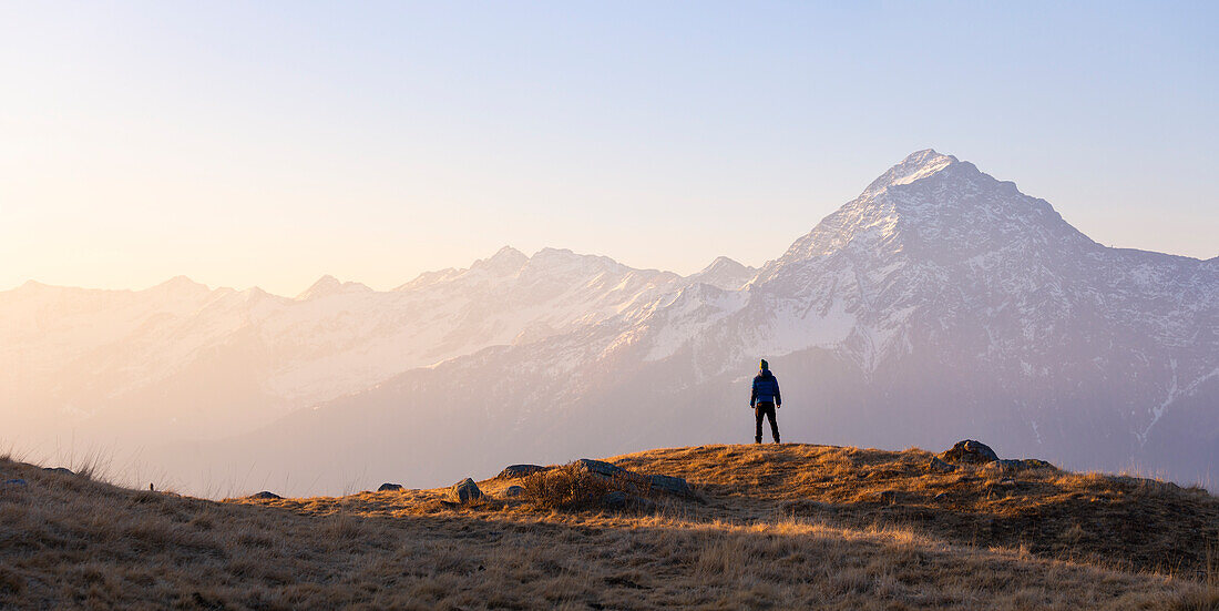 A trekker observes Monte Legnone at sunrise from Montemezzo, Alto Lario, Montemezzo, Como, Lombardy, Italy, Southern Europe