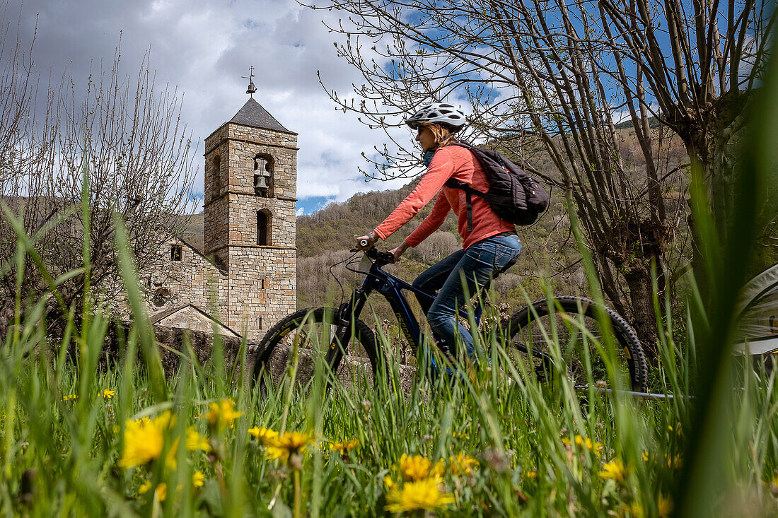 Frau auf Fahrrad und romanische Kirche von Sant Feliu, Barruera, Vall de Boí, Lleida, Katalonien, Spanien