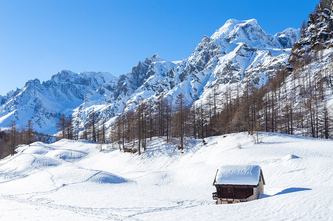 Blick auf eine Berghütte vor dem Monte Cervandone in der Kleinstadt Crampiolo im Winter. Alpe Devero, Antigorio-Tal, Piemont, Italien.