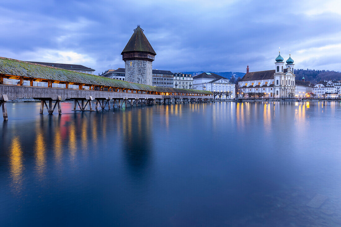 View of the Kapellbrücke bridge, the Jesuit Church and the Wasserturm at blue hour reflected on the Reuss river. Lucerne, canton of Lucerne, Switzerland.