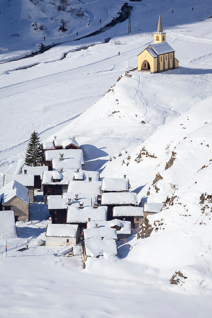 Blick auf die Kirche und das Dorf Riale im Winter von der Straße zur Maria-Luisa-Hütte und dem Hochtal von Formazza. Riale, Formazza, Valle Formazza, Verbano Cusio Ossola, Piemont, Italien.