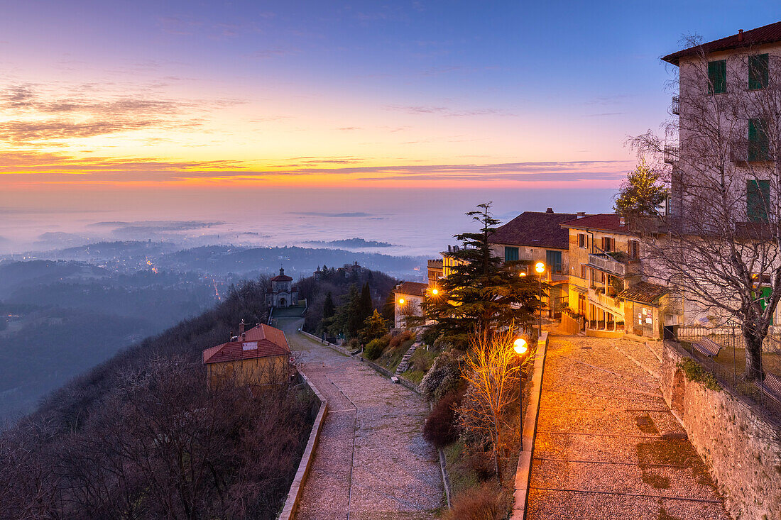 View of the old town of Santa Maria del Monte in winter at sunrise with the fog on Varese city and the Padana plain. Sacro Monte of Varese. Varese, Lombardy, Italy.