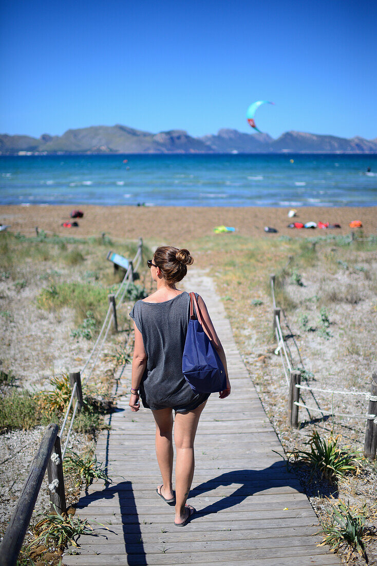 Young woman entering Port de Pollenca beach, ideal spot for practicing kitesurfing in Mallorca, Spain