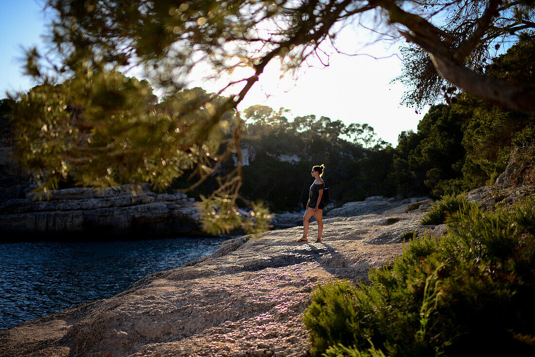 Junge Frau, umgeben von Natur, mit Blick auf den Horizont bei Sonnenuntergang an der Küste von Mallorca, Spanien