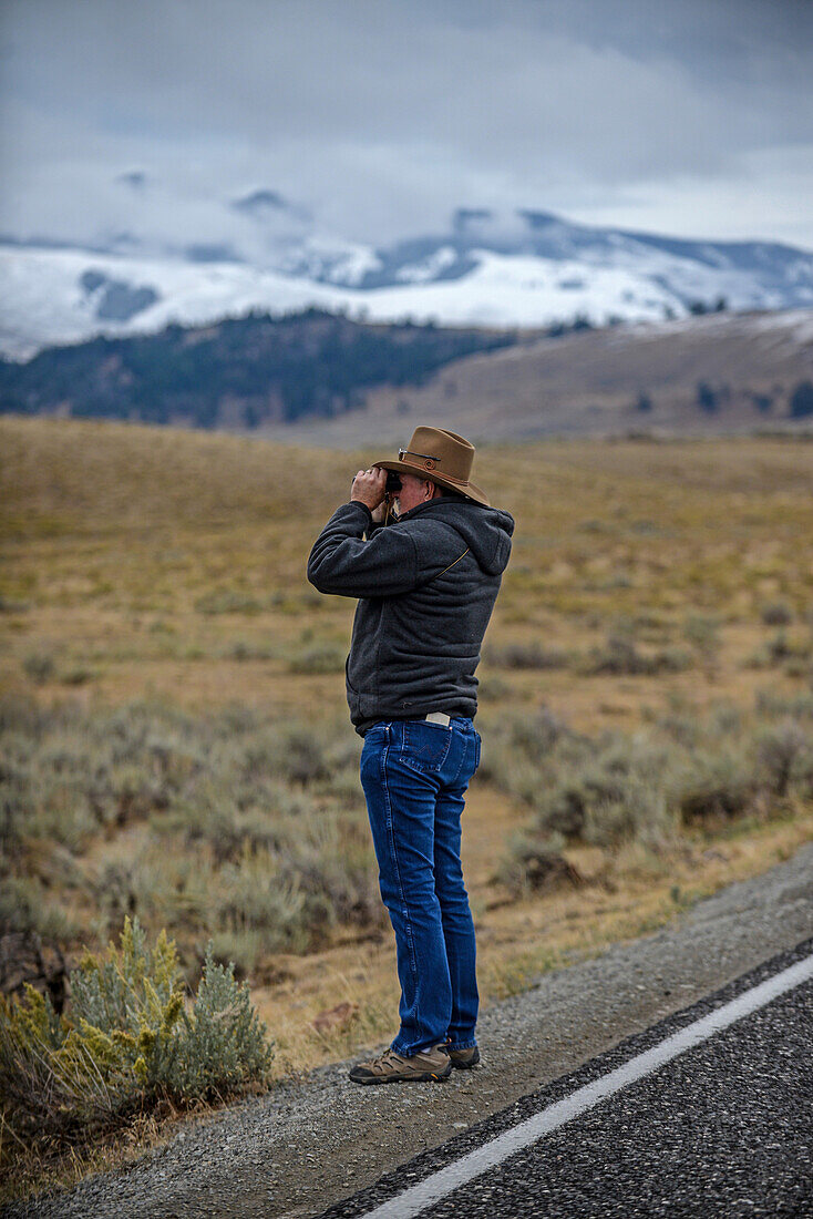 Mann beobachtet mit einem Fernglas die Tierwelt im Yellowstone-Nationalpark, USA