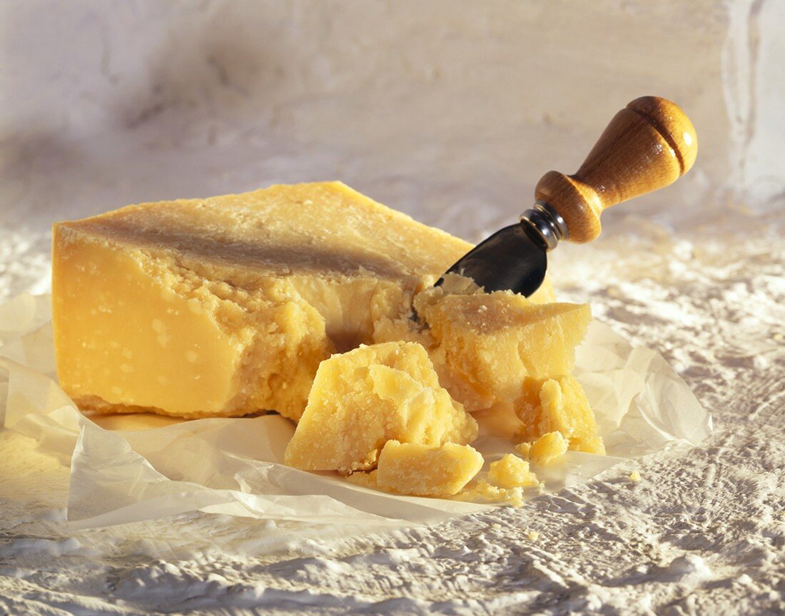 Stück Parmesan mit Käsemesser auf Papier auf Gips-Untergrund