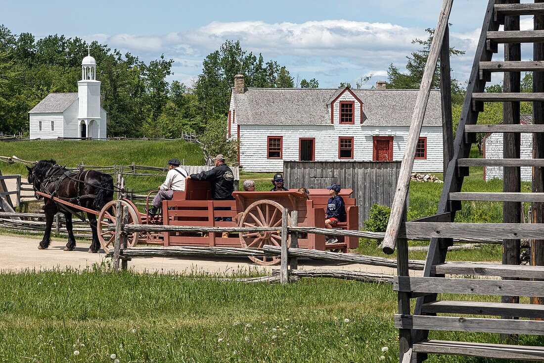 Ein historischer Wagen, der Touristen durch das Dorf fährt, die 1840 erbaute Blachall und die 1831 erbaute Kapelle, historisches Akadiendorf, Bertrand, New Brunswick, Kanada, Nordamerika