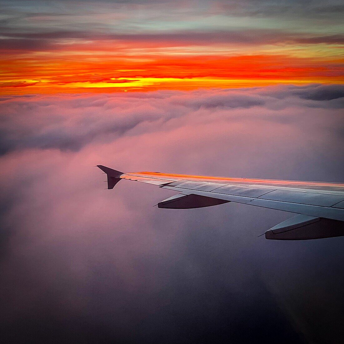 Wing of a plane at sunset over the clouds