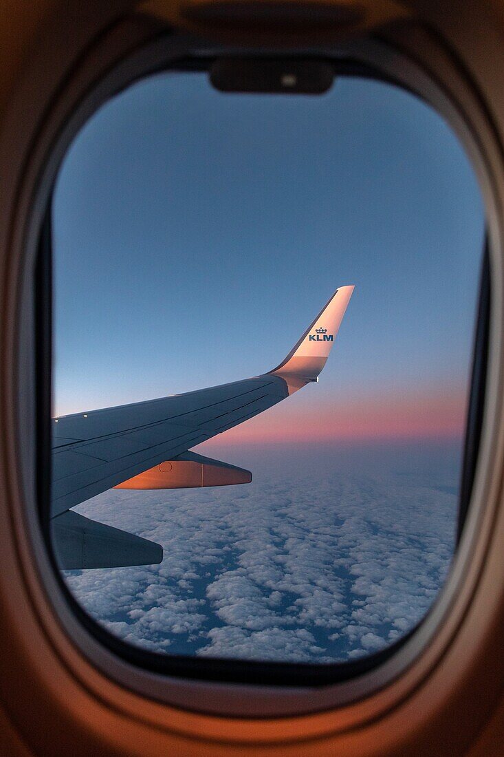 Flügel eines klm-Flugzeugs bei Sonnenuntergang über einem wolkenverhangenen Himmel