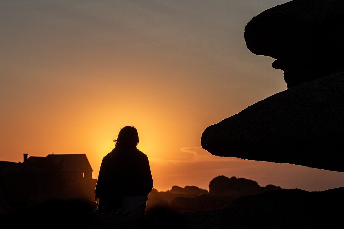 Frau auf den Felsen sitzend bei Sonnenuntergang, renote island point, tregastel, rosa Granitküste, cotes-d'armor, bretagne, frankreich