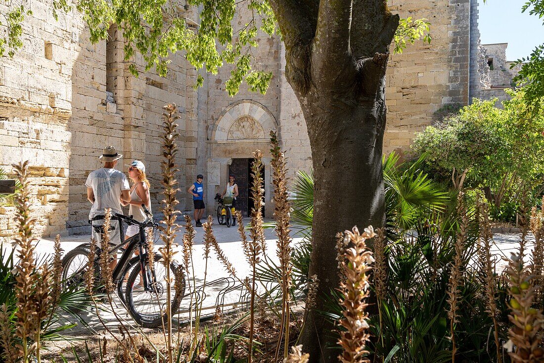Couple on bicycles in front of the entrance to the cathedral of maguelone, restored island church, villeneuve-les maguelone, herault, occitanie, france