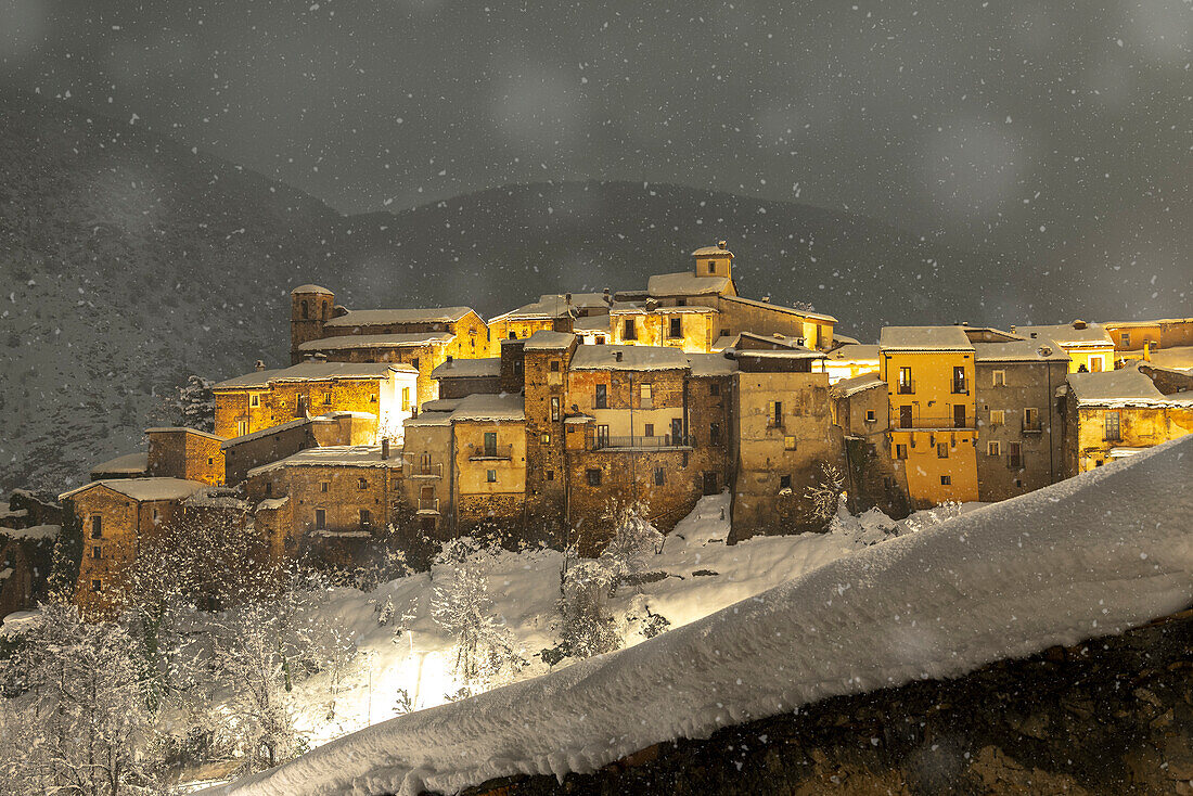 Nächtlicher Blick auf das beleuchtete Dorf Cansano bei starkem Schneefall, Provinz L'Aquila, Abruzzen, Italien