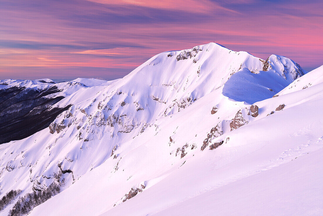 Winterlicher Blick bei Sonnenaufgang mit rosa Himmel auf den schneebedeckten Gipfel des Viglio, Apennin, Regionalpark Simbruini, Provinz Frosinone, Latium, Italien