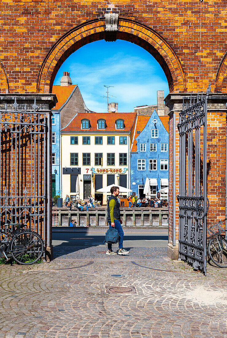 Blick auf einen Mann, der durch einen Bogen aus Ziegelsteinen auf der Straße der bunten Gebäude des Stadtteils Nyhavn spazieren geht, Kopenhagen, Hovedstaden Dänemark, Europa