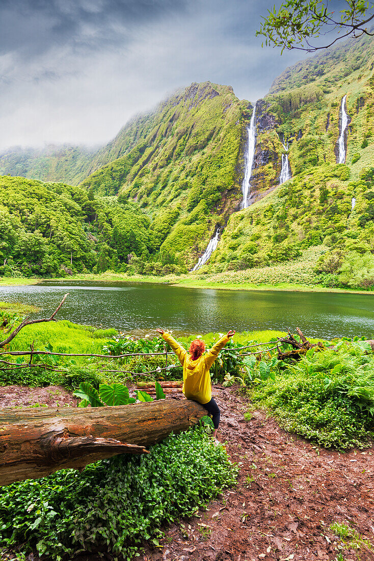 Woman enjoys the scenic view of the waterfall of Ribeira do Ferreiro among lush vegetation, Poco Ribeira do Ferreiro (Alagoinha), Lajes das Flores municipality, Flores Island (Ilha das Flores), Azores archipelago, Portugal, Europe