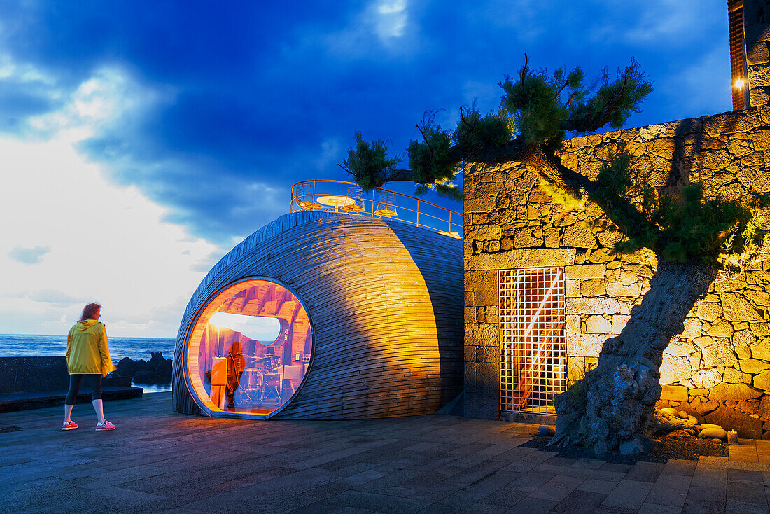 Woman standing in front of an exclusive cafe with reflection at dusk, Madalena, Madalena municipality, Pico island (Ilha do Pico), Azores archipelago, Portugal, Europe