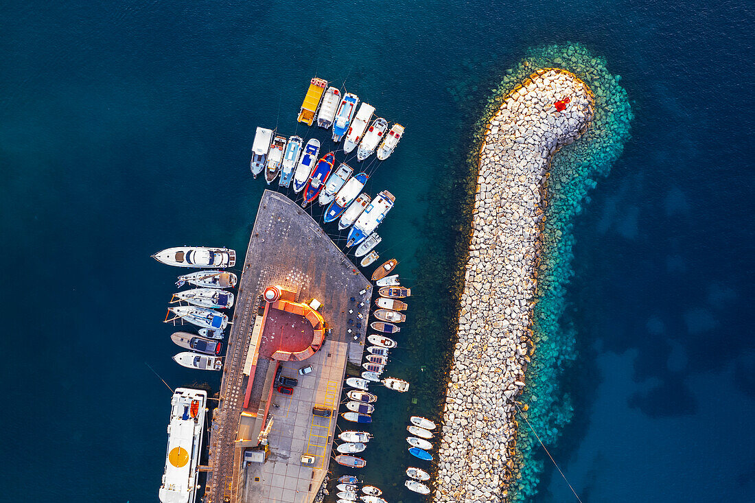 Luftaufnahme von bunten Booten und Fischerbooten im türkisfarbenen Wasser des Hafens von Ponza mit dem Leuchtturm und den Felsen bei Sonnenuntergang, Insel Ponza, Archipelago Pontino, Provinz Latina, Latium, Italien