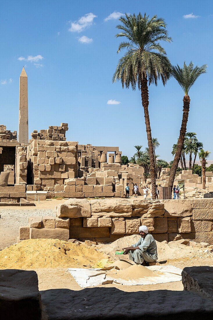 Mann siebt Sand in der hellen Sonne, Ruinen und Obelisk, Bezirk von Amun-Re, Tempel von Karnak, antike ägyptische Stätte aus der 13. Dynastie, unesco weltkulturerbe, luxor, ägypten, afrika