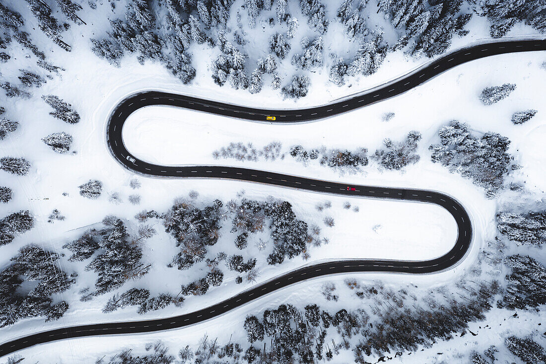 Aerial view of the s-shape mountain road along the winter forest covered with snow