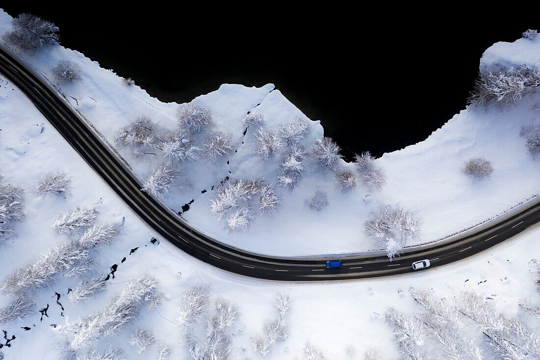 Luftaufnahme von Autos in den Kurven der verschneiten Straße am Ufer des Silsersees, Kanton Graubünden, Engadin, Schweiz