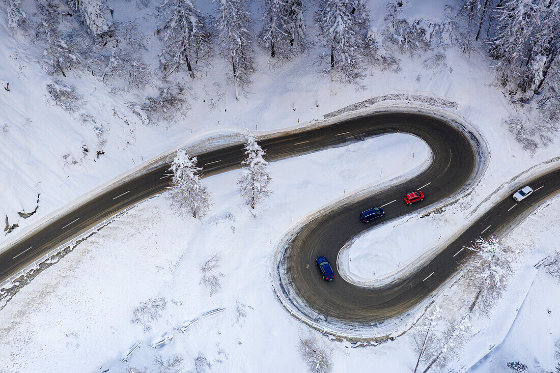 Luftaufnahme von Autos in den Kurven einer verschneiten Bergstraße im Winter