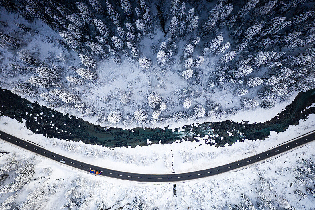 Schneepflug auf Bergstraße im verschneiten Wald am Ufer des gefrorenen Flusses, Luftbild, Zernez, Engadin, Schweiz