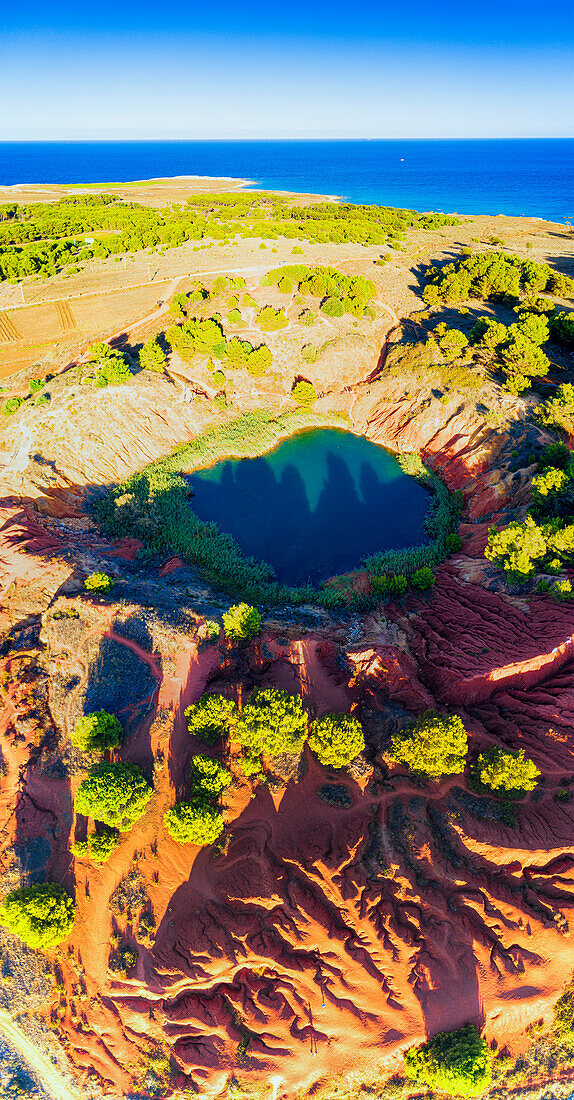 Red rocks and emerald lake of abandoned bauxite quarry with sea on background, Otranto, Lecce province, Apulia, Italy