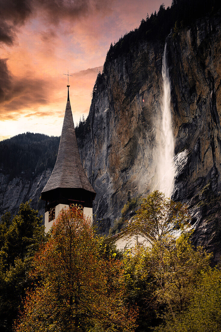 Sonnenaufgang über dem fließenden Wasser des Staubbachfalls und dem Glockenturm, Lauterbrunnen, Berner Oberland, Kanton Bern, Schweiz