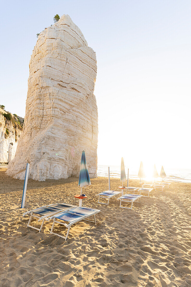 Rock formation of Pizzomunno and sunbeds at dawn, beach of Castello, Vieste, Foggia province, Gargano, Apulia, Italy