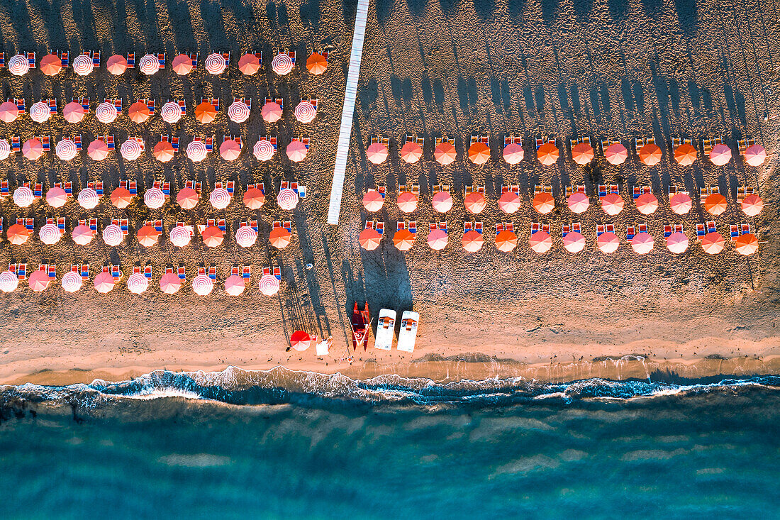 Aerial view of beach umbrellas in a row on sand beach washed by waves, Vieste, Foggia province, Gargano, Apulia, Italy